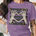 Skeleton hands forming a heart on a purple t-shirt with stars.