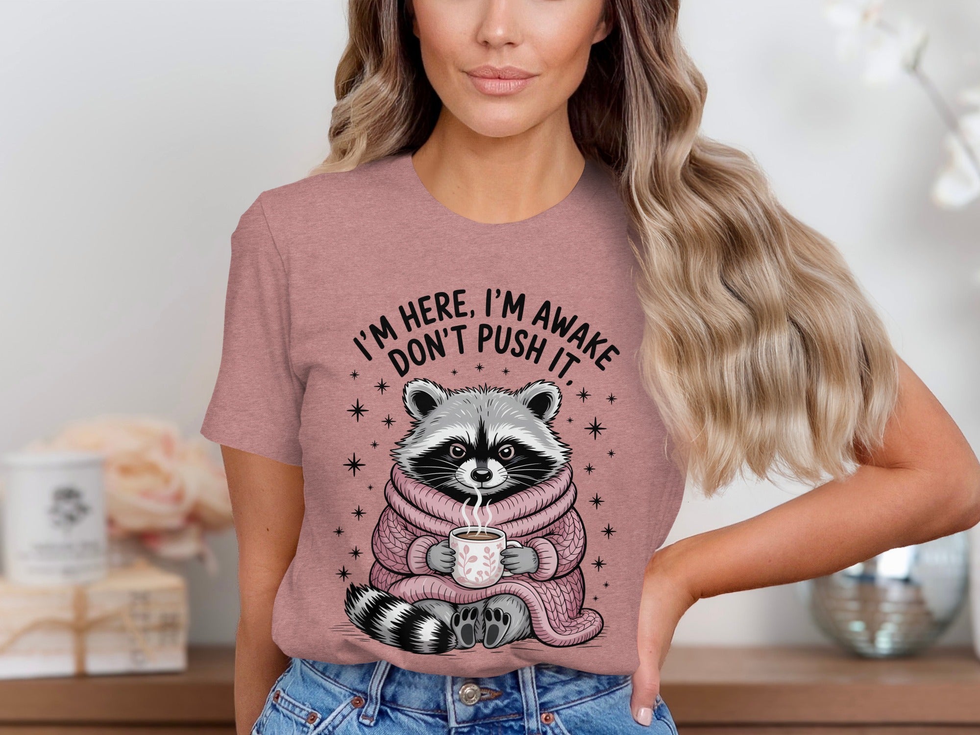 Raccoon in a pink scarf holding a coffee mug with text: I'm here, I'm awake, don't push it.