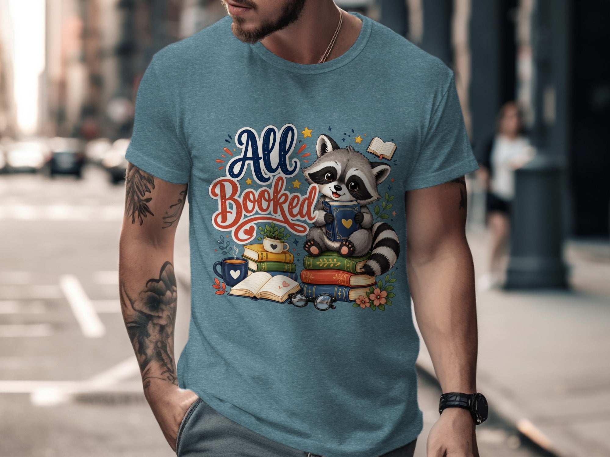 T-shirt graphic featuring a raccoon reading a book, surrounded by stacked books and text "All Booked".